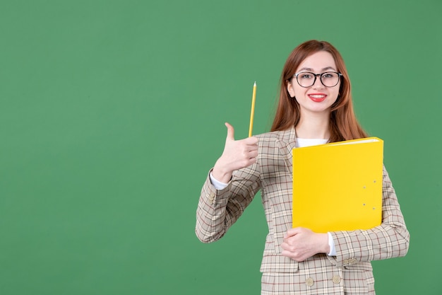 Ritratto di insegnante femminile in posa con file giallo e matita sorridente su green