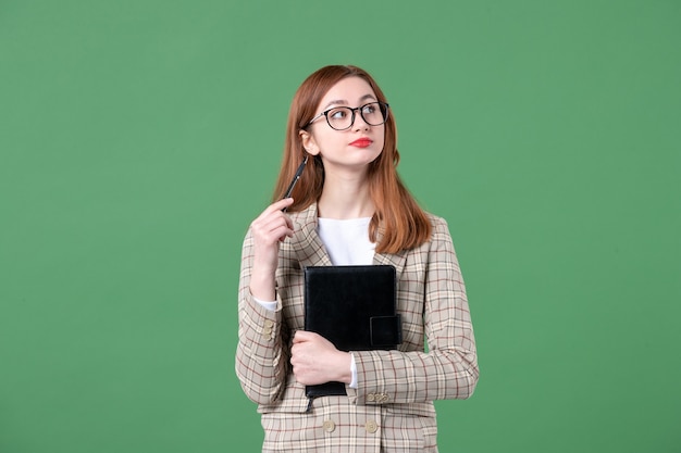 Ritratto di insegnante femminile in tuta con blocco note e penna su verde