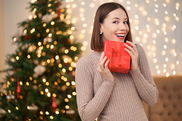 Ritratto di labbra rosse di giovane donna felice in posa con una confezione regalo avvolta.