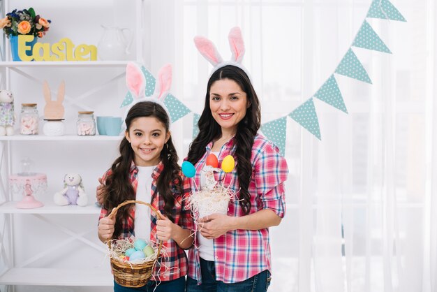 Ritratto di madre e figlia con le orecchie di coniglio tenendo in mano le uova di Pasqua colorate