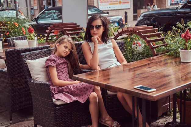 Ritratto di mamma alla moda e della sua adorabile figlia durante un periodo in un caffè all'aperto. Felice famiglia alla moda.