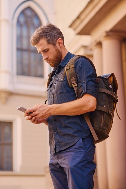 Ritratto di maschio hipster barbuto che utilizza smartphone all'aperto.