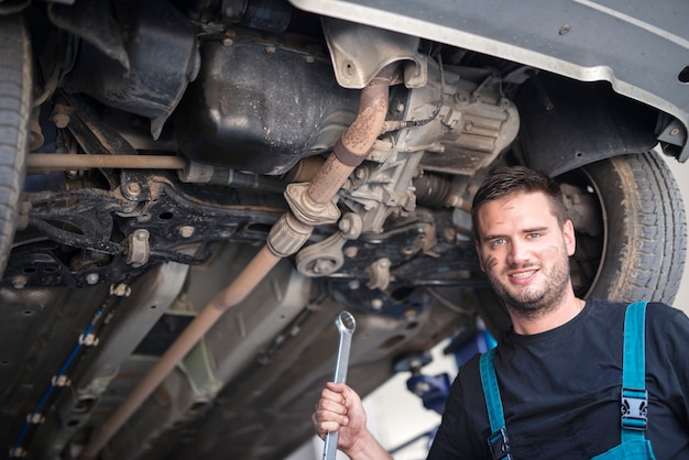 Ritratto di meccanico di auto con strumento chiave che lavora sotto il veicolo in officina di riparazione auto