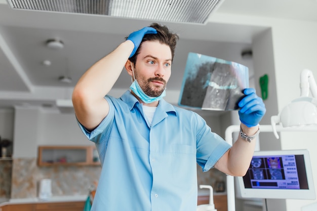 Ritratto di medico o dentista maschio barbuto con faccia emotiva guardando i raggi x, nel suo ufficio moderno.