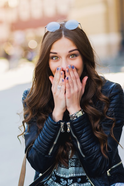 Ritratto di moda all'aperto di elegante giovane donna divertirsi, faccia emotiva, ridendo. Stile di strada urbano della città. Vestito primaverile o autunnale.