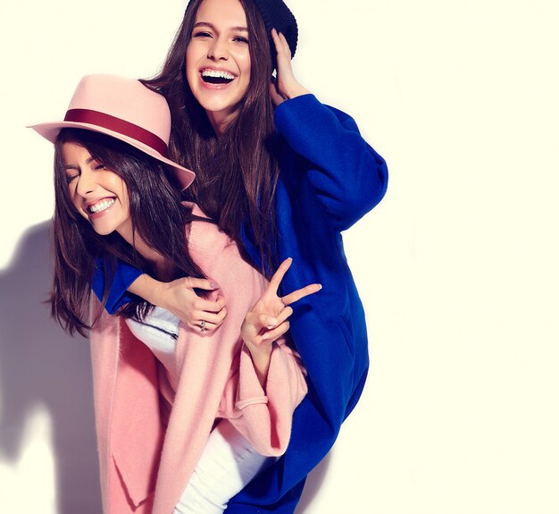 ritratto di moda di due modelli sorridenti delle donne del brunette in cappotto casuale dei pantaloni a vita bassa di estate isolato su bianco. Ragazze che si tengono sulla schiena