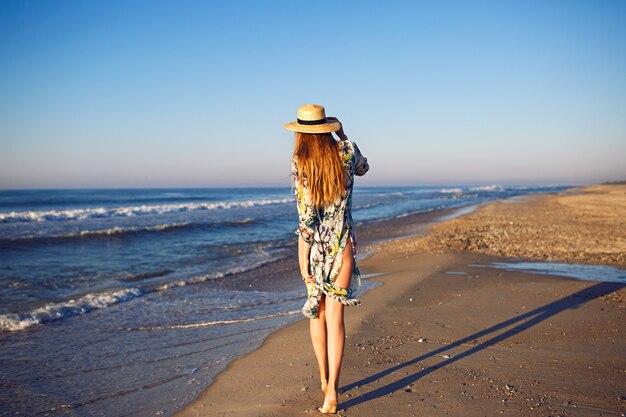 Ritratto di moda estate all'aperto del modello biondo in posa vicino all'oceano in spiaggia solitaria, colori tonica, rilassante vacanza di lusso