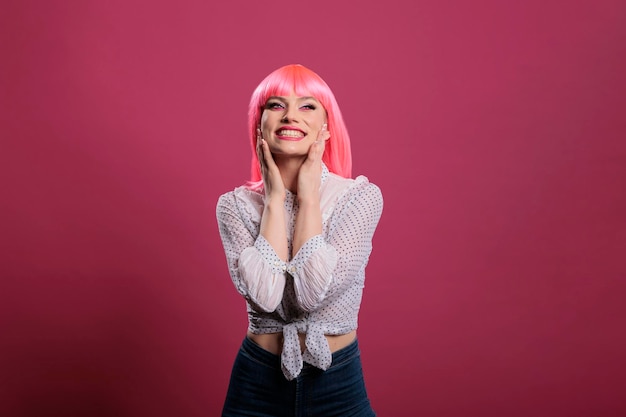 Ritratto di modello glamour sorridente e in posa sulla fotocamera, felice e positivo in studio. Donna gioiosa spensierata con parrucca di capelli rosa e trucco elegante che fa mosse sensuali e attraenti.