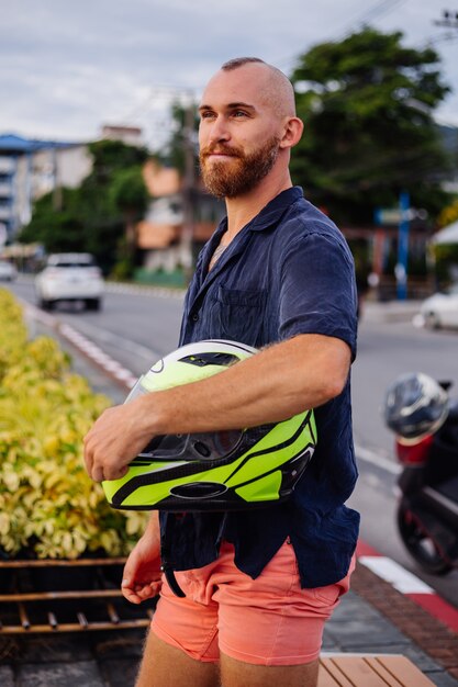 Ritratto di motociclista maschio con casco giallo seduto su una panchina sul lungomare in Thailandia al tramonto