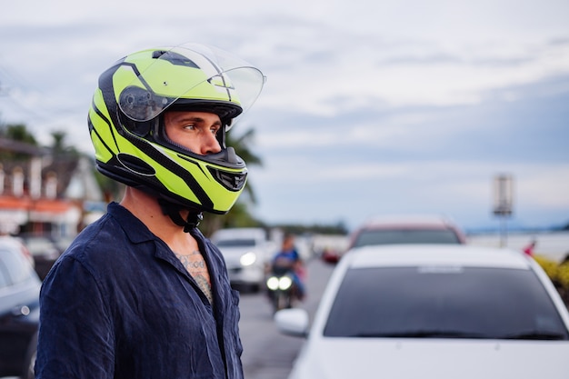 Ritratto di motociclista maschio in casco giallo sul lato della strada trafficata in Thailandia al tramonto