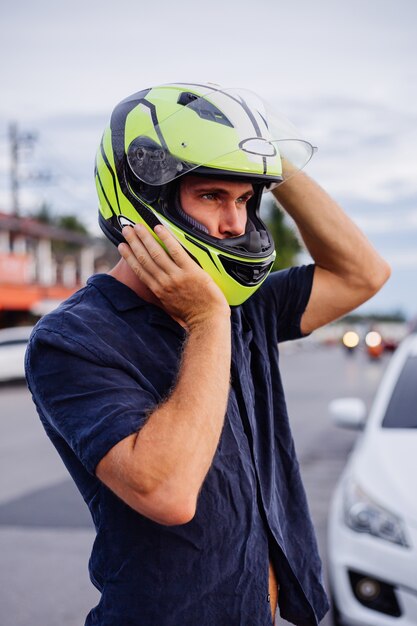 Ritratto di motociclista maschio in casco giallo sul lato della strada trafficata in Thailandia al tramonto