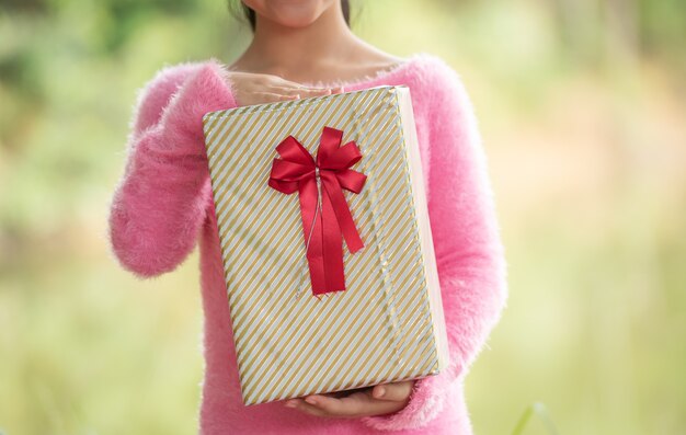 Ritratto di Natale di una bambina sorridente felice con una confezione regalo vicino a un albero verde del ramo. foglie verdi bokeh fuori fuoco sfondo dalla foresta naturale.