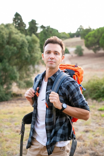 Ritratto di pensieroso viaggiatore maschio in piedi sulla natura. Uomo caucasico bello che viaggia e che trasporta zaino. Concetto di turismo, avventura e vacanze estive con lo zaino in spalla