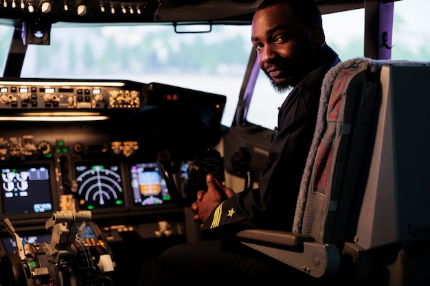 Ritratto di pilota afroamericano che utilizza il comando del cruscotto in cabina per il decollo con un aereo jet e volare. Aviatore maschio in uniforme delle vie aeree che spinge i pulsanti del pannello di controllo e la leva di alimentazione.