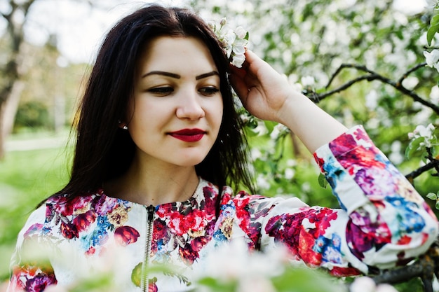Ritratto di primavera di ragazza bruna al giardino di fiori verdi