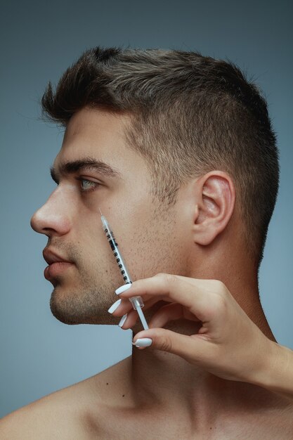 Ritratto di profilo del primo piano di giovane uomo isolato su sfondo grigio studio. Procedura chirurgica di riempimento. Concetto di salute e bellezza maschile, cosmetologia, cura di sé, cura del corpo e della pelle. Anti età.