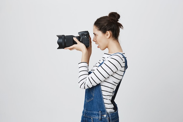 Ritratto di profilo di bella ragazza fotografo guardando attraverso l'obiettivo della fotocamera, scattare foto