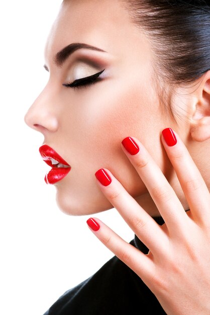 Ritratto di profilo di una bellissima giovane donna con rossetto rosso. Modello di moda con brillante manicure glamour.