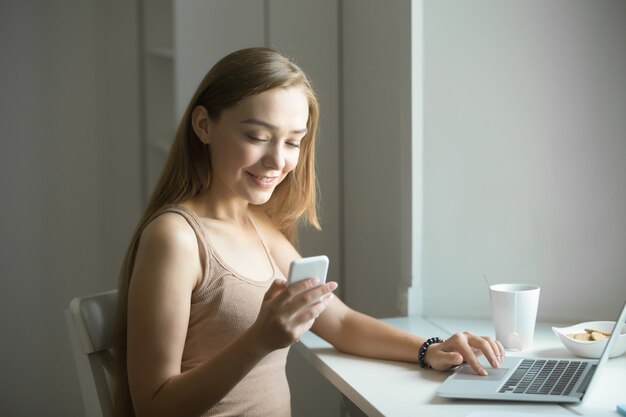 Ritratto di profilo di una giovane donna, telefono in mano, laptop vicino