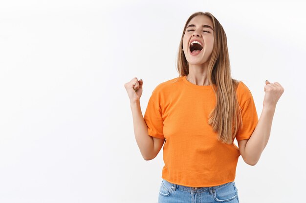 Ritratto di ragazza bionda sollevata e autorizzata, studentessa che grida sì in cielo, chiude gli occhi e sorride dalla felicità e gioisce, pompa a pugno, trionfa sulla vittoria, celebra la vittoria o il successo