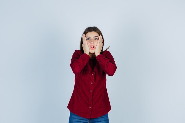 Ritratto di ragazza che si tiene per mano sulle guance in camicia casual e sembra ansiosa