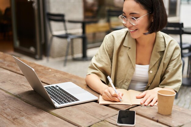 Ritratto di ragazza concentrata che fa i compiti frequentando un corso online che prende appunti mentre si lavora su l