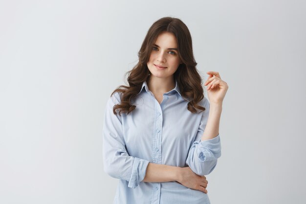 Ritratto di ragazza giovane studente con capelli scuri ondulati in camicia blu con sguardo sicuro e sorriso gentile.