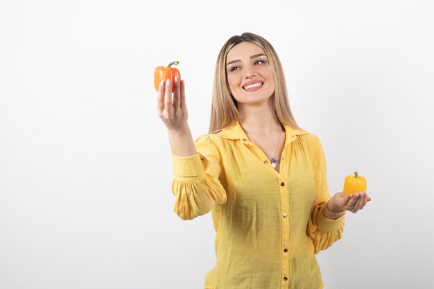 Ritratto di ragazza positiva che offre peperoni colorati sul muro bianco.