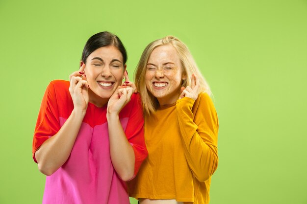 Ritratto di ragazze abbastanza affascinanti in abiti casual isolati su sfondo verde studio. Due modelli femminili come fidanzate o lesbiche. Concetto di LGBT, uguaglianza, emozioni umane, amore, relazione.