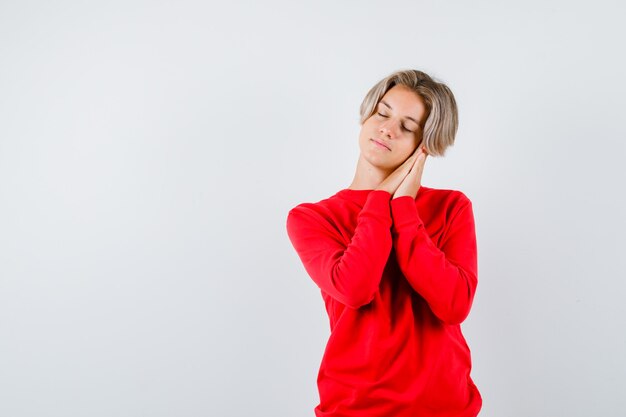 Ritratto di ragazzo adolescente appoggiato sui palmi come cuscino in maglione rosso e guardando assonnato vista frontale