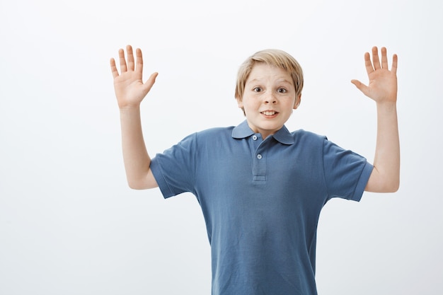 Ritratto di ragazzo adolescente felice positivo in maglietta blu alzando le palme in alto nella resa di essere sorpreso e catturato da un amico mentre gioca in cortile