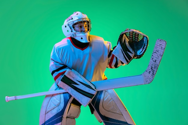 Ritratto di ragazzo adolescente giocatore di hockey che gioca isolato su sfondo verde in luce al neon