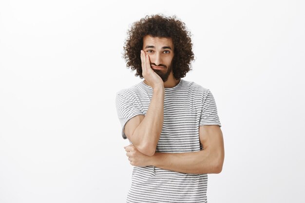 Ritratto di ragazzo ispanico infastidito triste con acconciatura afro fresca, viso appoggiato sul palmo e guardando con occhi stanchi