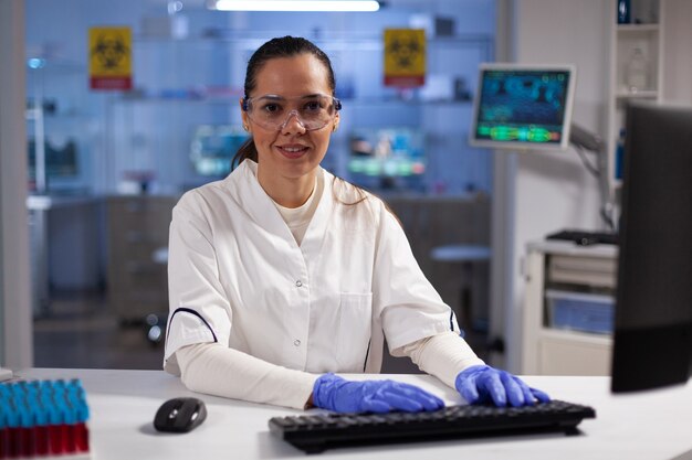 Ritratto di ricercatore biochimico digitando competenze biochimiche sul computer che lavora all'esperimento medico nel laboratorio ospedaliero di microbiologia. Medico terapista che sviluppa un vaccino contro il coronavirus