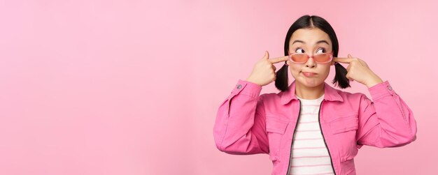 Ritratto di sciocca ragazza giapponese chiude le orecchie guarda da parte non ascolta non riesco a sentirti gesto in piedi su sfondo rosa ignorandoti