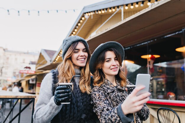 Ritratto di selfie di donne alla moda gioiose divertendosi sulla strada soleggiata in città. Look elegante, divertimento, viaggio con gli amici, sorriso, espressione di vere emozioni positive.