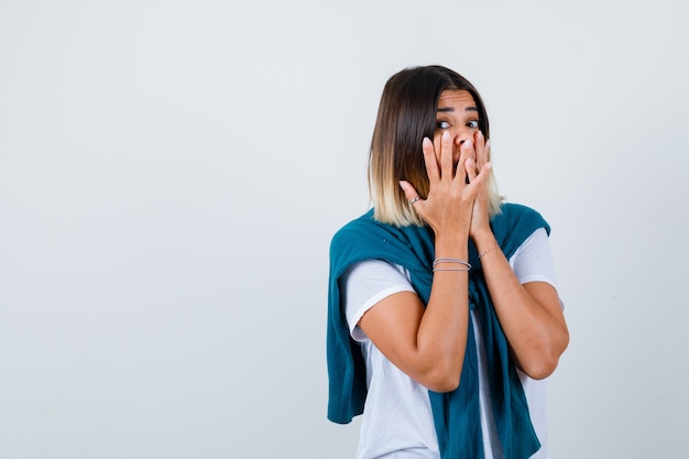 Ritratto di signora con un maglione legato che copre la bocca con le mani in una maglietta bianca e sembra spaventata vista frontale