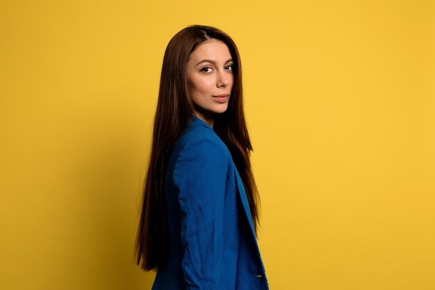 ritratto di signora piuttosto affascinante con lunghi capelli scuri che indossa giacca blu sul muro giallo