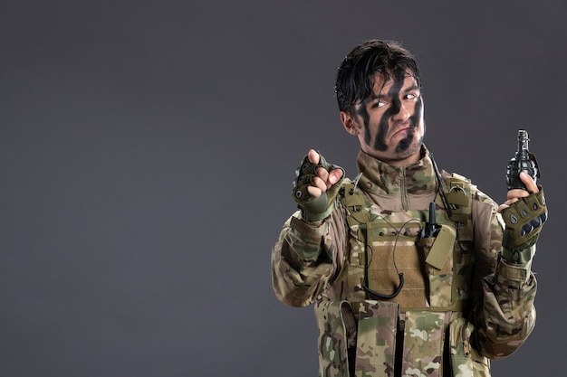 Ritratto di soldato maschio in mimetica con granata sul muro scuro
