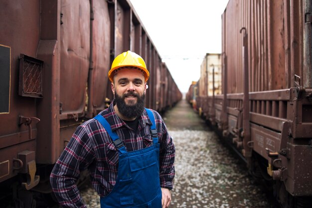 Ritratto di sorridente operaio ferroviario in piedi tra i treni merci