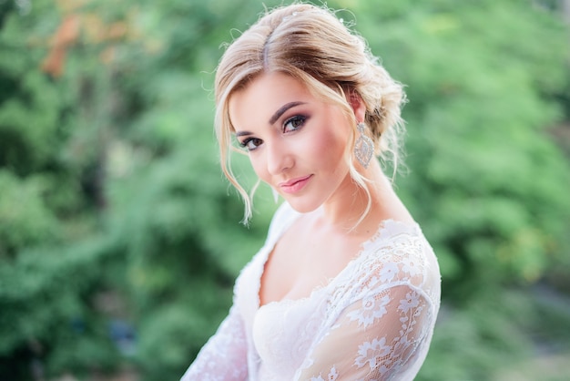 Ritratto di splendida bionda sposa in piedi sul balcone prima di alberi verdi