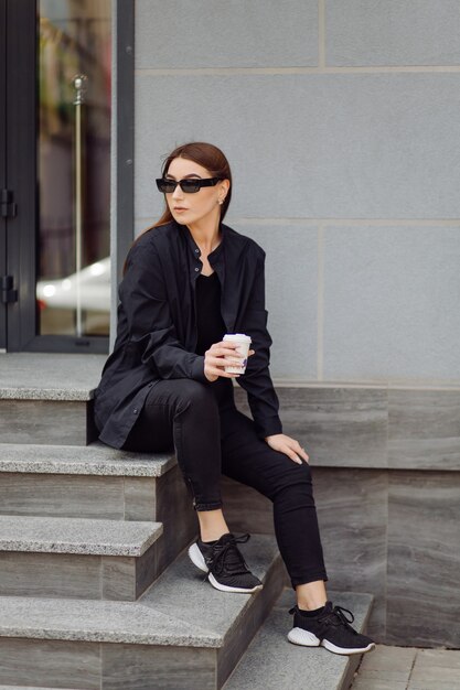 Ritratto di stile di vita all'aperto di splendida ragazza bruna. Bere caffè e camminare per le strade della città.