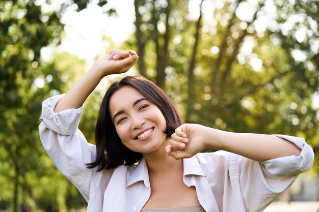 Ritratto di stile di vita della gente di giovane donna bruna che balla sorridente e ridendo camminando nel parco con