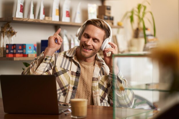 Ritratto di stile di vita di un uomo nomade digitale sorridente in un caffè che lavora su un portatile ascoltando musica in