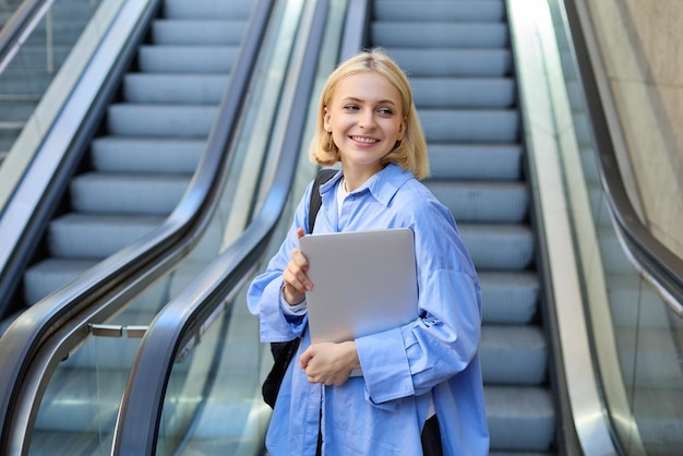 Ritratto di stile di vita di una giovane donna con un laptop che si allontana dall'escalator verso la metropolitana