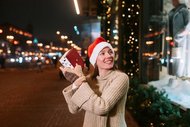 Ritratto di strada di notte di giovane bella donna che agisce entusiasta. Luci festive della ghirlanda.