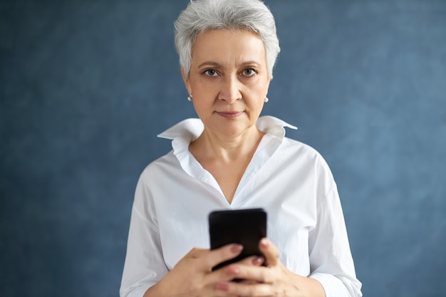 ritratto di successo dirigente femminile di mezza età con corti capelli grigi digitando un messaggio di testo sul suo telefono cellulare