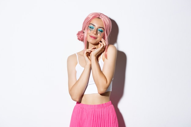 Ritratto di tenera ragazza alla moda in parrucca rosa, chiudere gli occhi e toccare delicatamente il viso