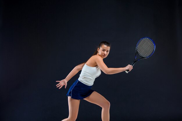 Ritratto di tennis bella ragazza con una racchetta sulla parete scura