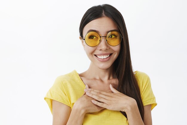 Ritratto di toccata e compiaciuta donna europea arrossendo in occhiali da sole gialli alla moda tenendo le palme per la gioia